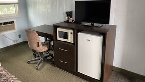 A compact office space with a desk, chair, microwave, refrigerator, and a television.