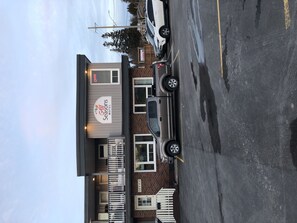 Un motel avec une enseigne indiquant « Seasons Motel ». Plusieurs véhicules sont stationnés devant, et le bâtiment présente une façade en briques, avec une clôture blanche à l’avant.