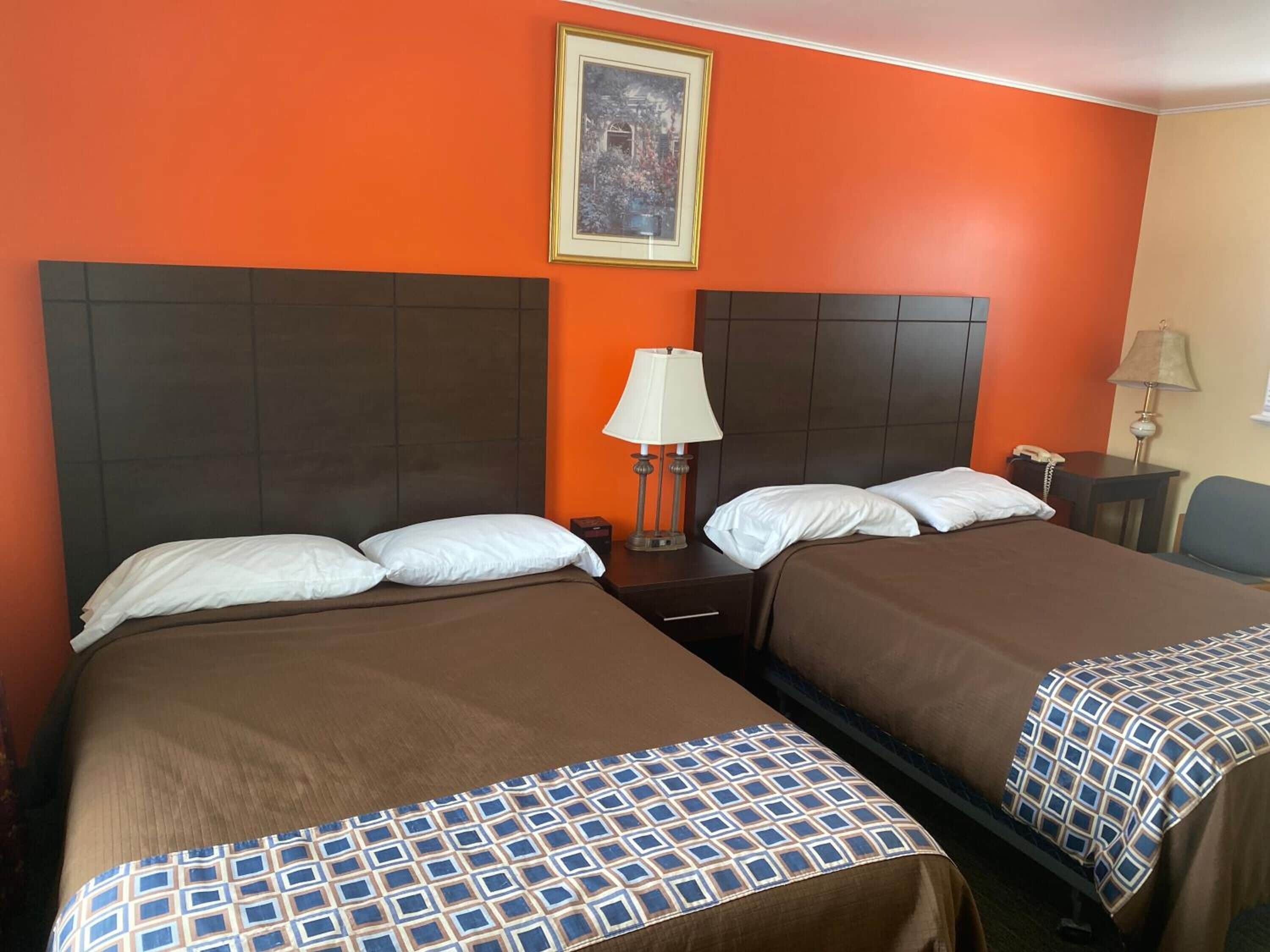 Habitación de hotel con dos camas, cada una con una colcha marrón y almohada estampada. Encima de las camas hay un cuadro enmarcado, una mesita de noche con una lámpara y una pequeña mesa con un teléfono.