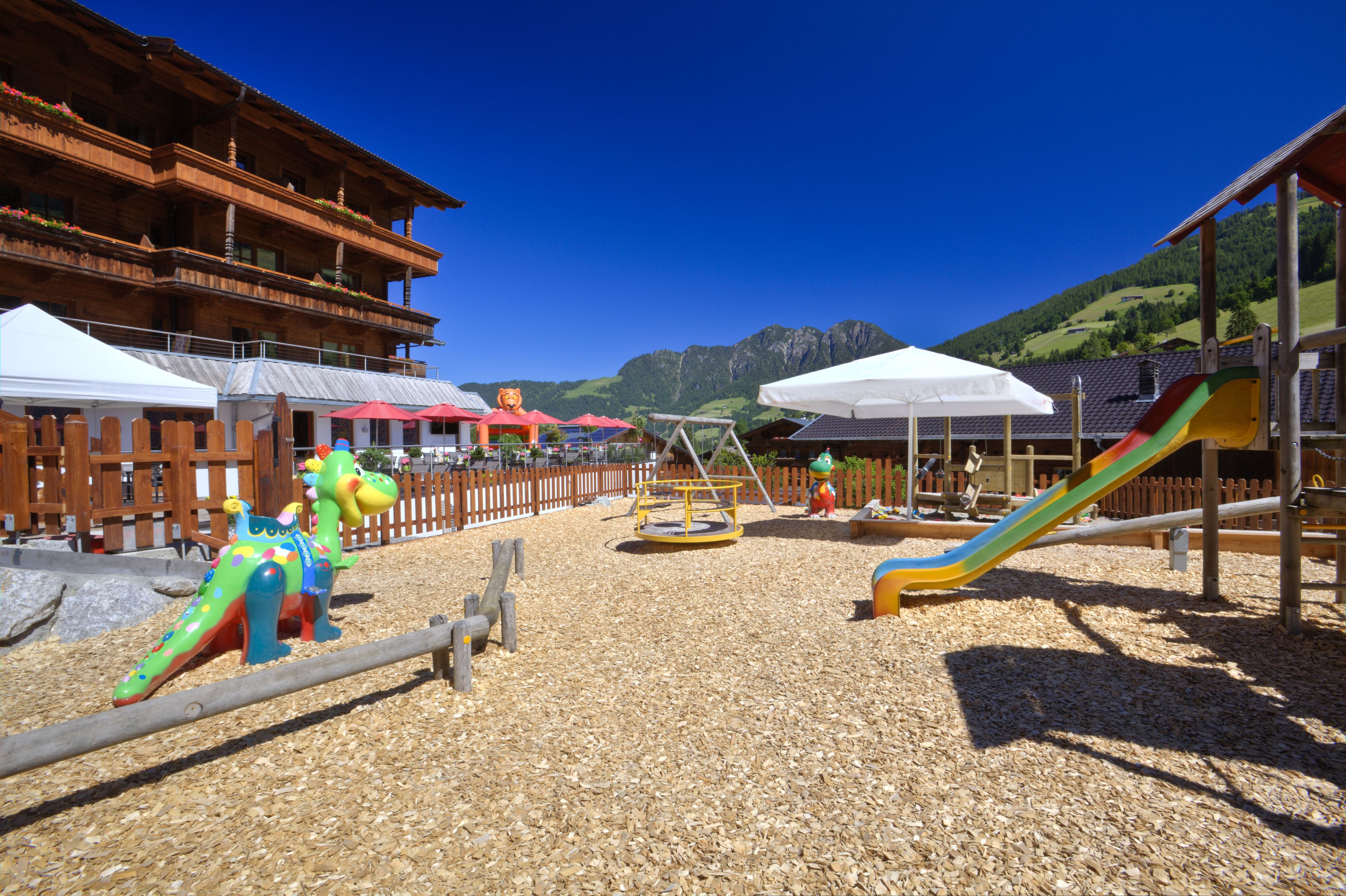 Un parque infantil con una estructura de madera para escalar, un tobogán y una zona de juegos con valla de madera.