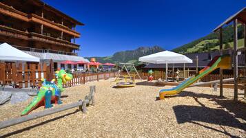 Un parque infantil con una estructura de madera para escalar, un tobogán y una zona de juegos con valla de madera.