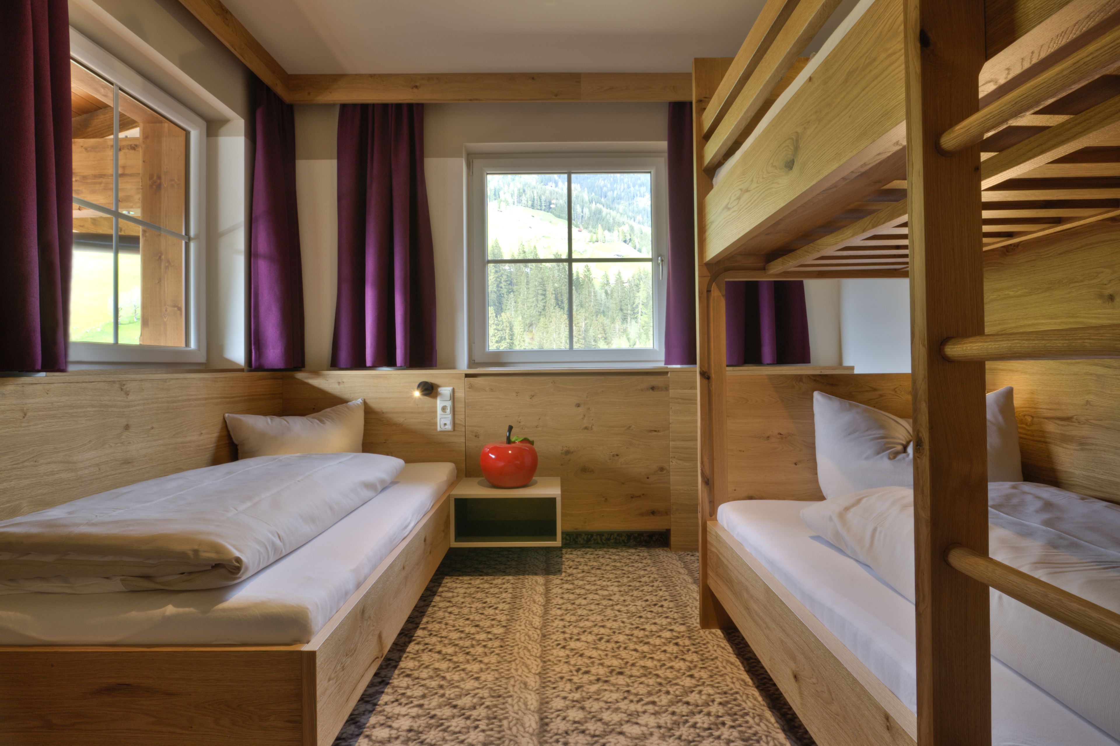 Habitación de cabaña de madera con literas, una ventana con vistas a un bosque y una mesita con una manzana roja.