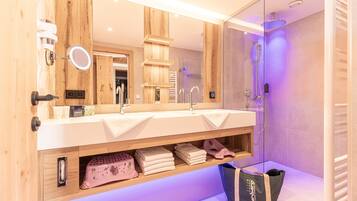 A modern bathroom with a wooden vanity, dual sinks, a glass shower enclosure, and a visible towel rack.