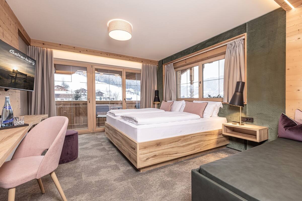 A modern hotel room with a wooden bed, a desk, a chair, and a TV on the wall.