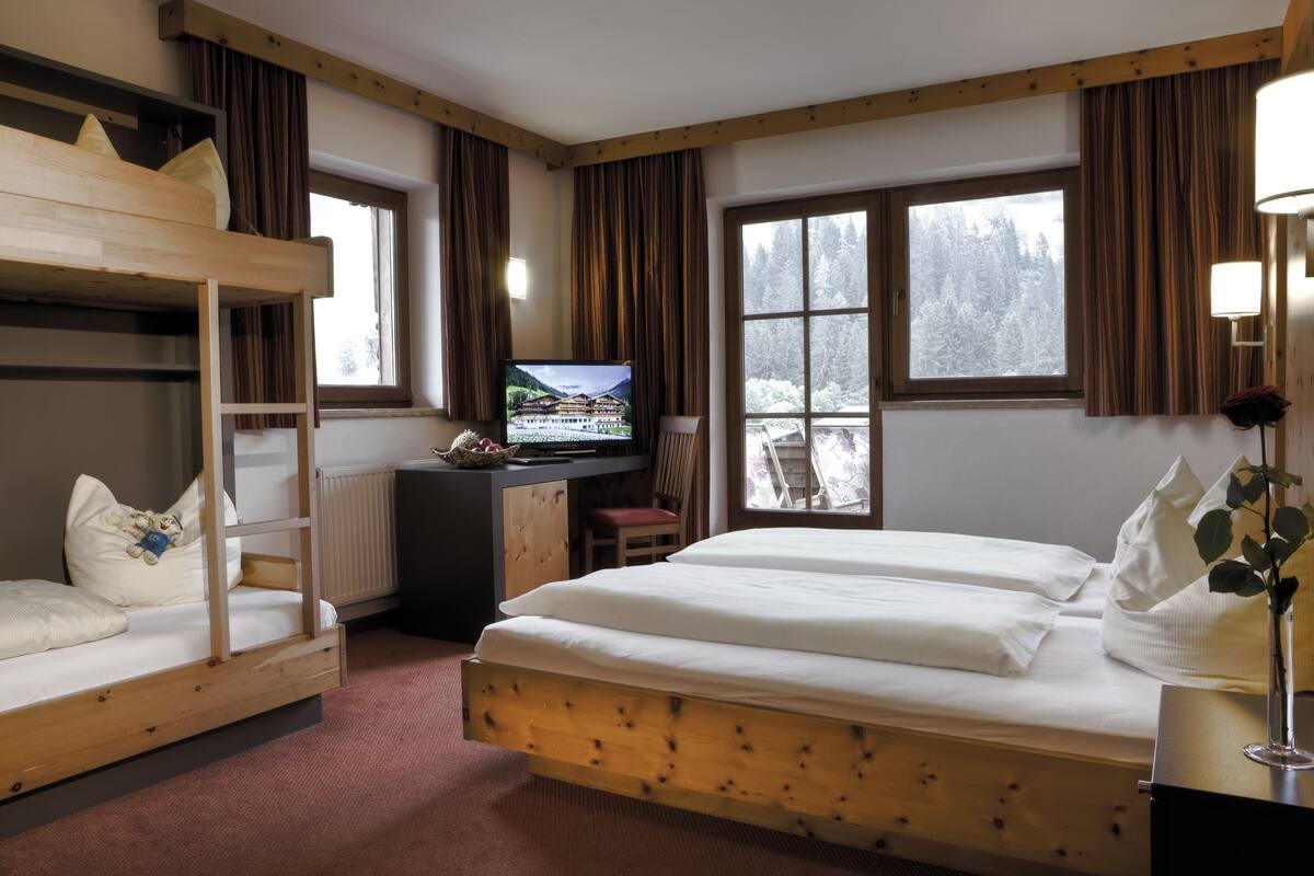 A room with a bunk bed, a desk with a computer, a chair, and a window with a view of trees.