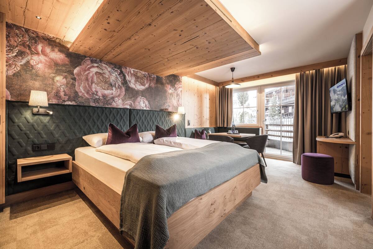 A modern hotel room with a large bed, a desk, a chair, a TV, and a window with curtains.