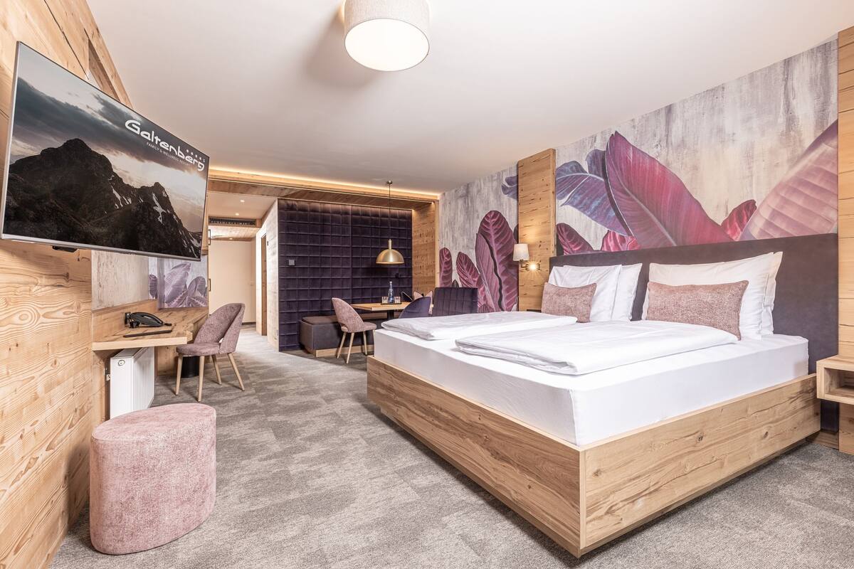 A modern hotel room with a large bed, a desk, a chair, and a television on the wall.
