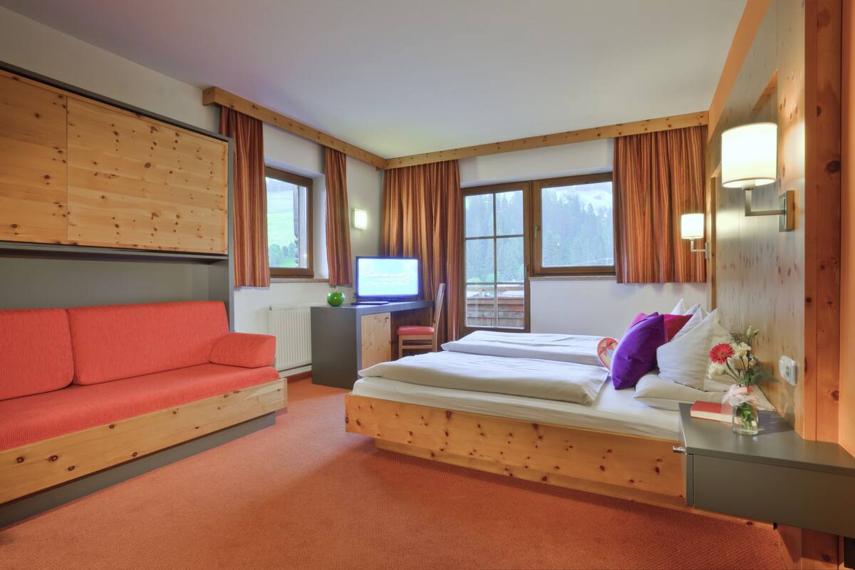 A room with a bed, a red sofa, a television, and a window with curtains.