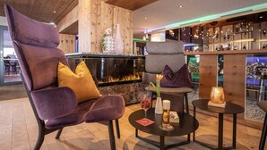 A modern lounge area with plush seating, a fireplace, and a bar with various bottles. - Galtenberg Family & Wellness Resort (Alpbach)