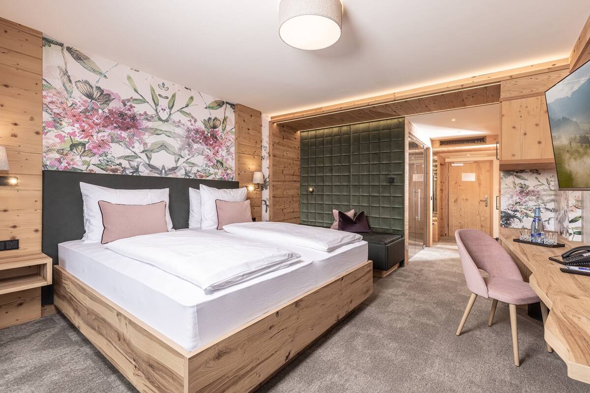 A modern bedroom with a wooden bed, a desk, and a large floral wall mural.