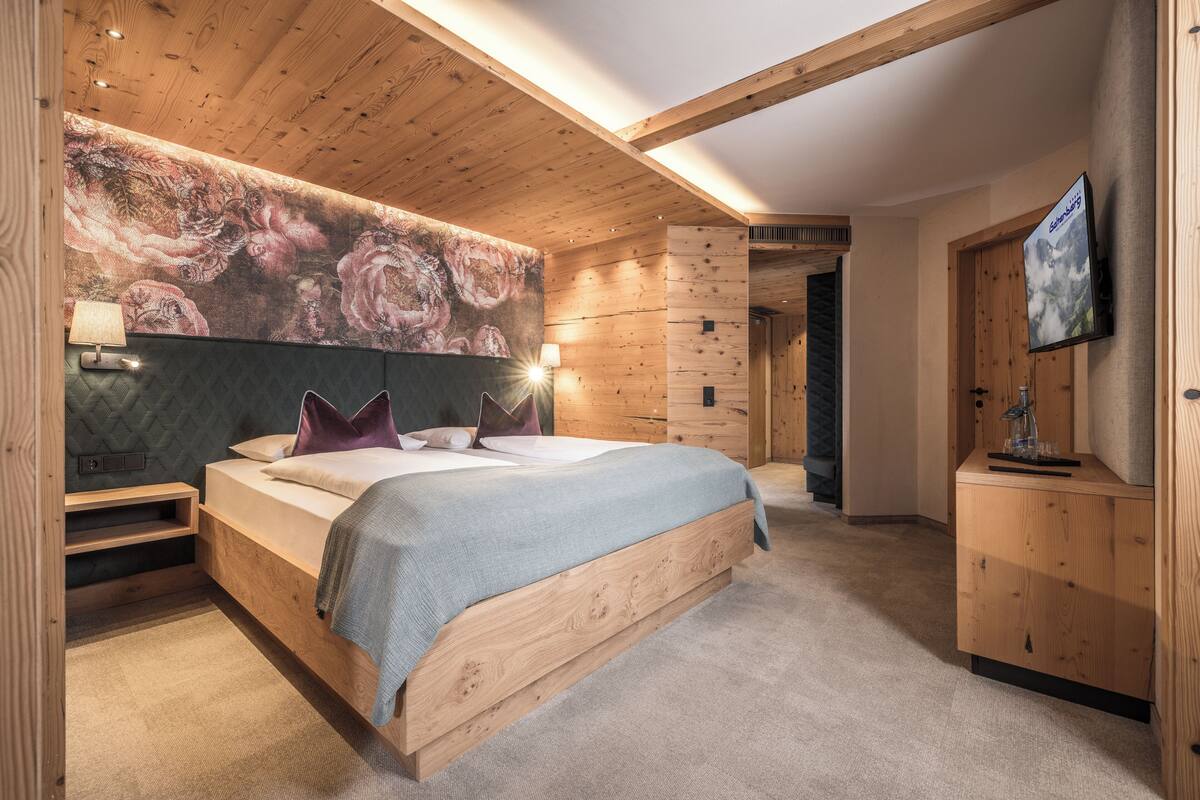A modern bedroom with a large bed, wooden headboard, and a wall-mounted TV.