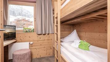 A wooden cabin room with a bunk bed, a small desk with a computer, a window with a view of a mountain, and a radiator.