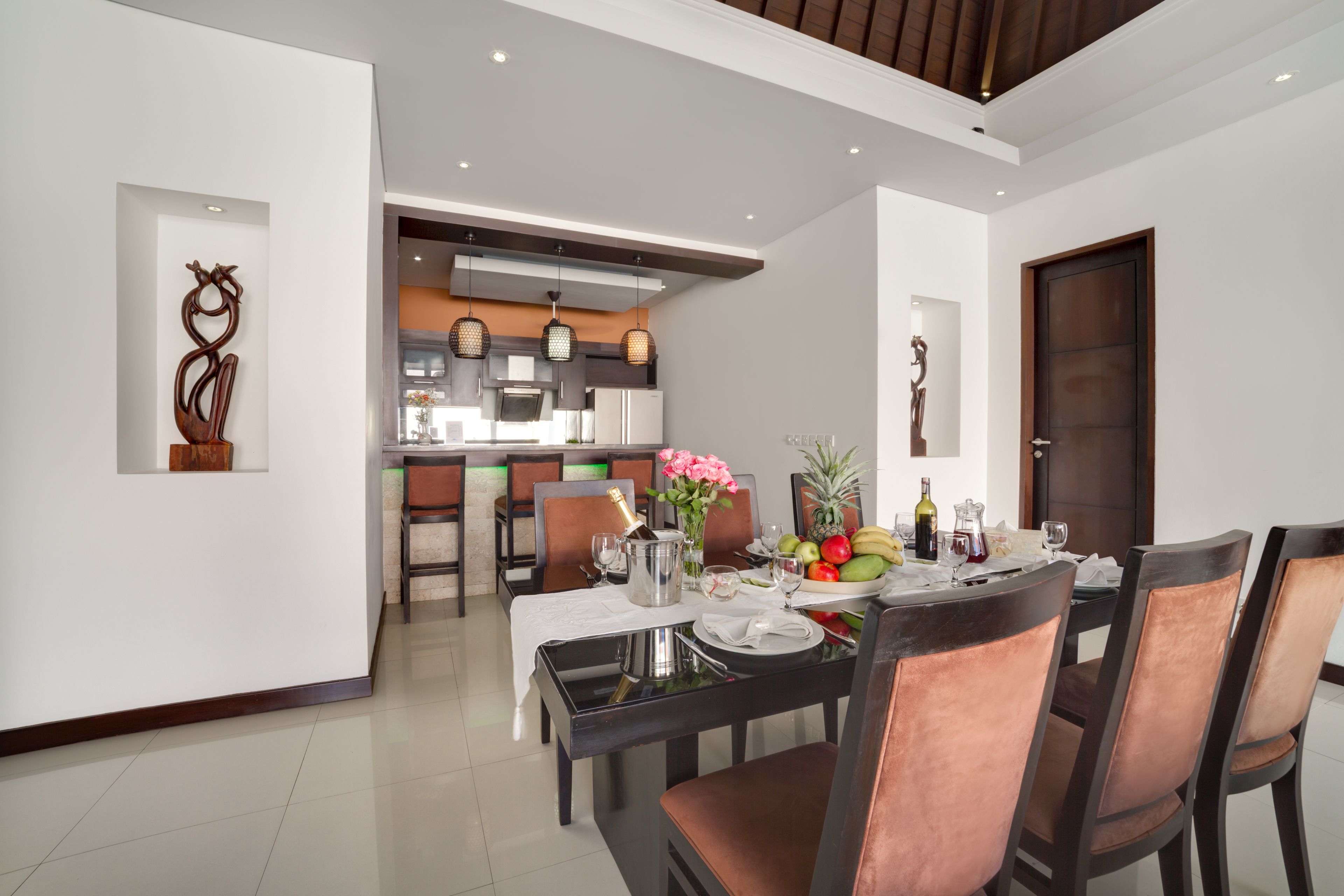 A modern dining area with a table set for four, a kitchen in the background, and a wooden door.