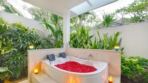 A spa area with a hot tub filled with red pebbles, surrounded by lush greenery and ambient lighting. - D&G Villas (Nusa Dua)