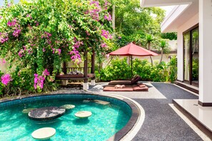 Une piscine dont le bord est recouvert de carrelage, entourée d’un jardin agrémenté de fleurs roses et d’un parasol rouge.
