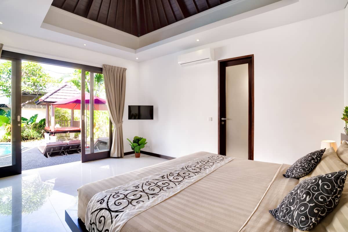 A modern bedroom with a large bed, a TV, and a sliding glass door leading to an outdoor area.