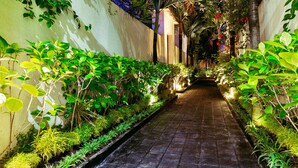 A narrow, paved pathway flanked by lush greenery and architectural elements, suggesting a tranquil, well-maintained garden or courtyard area. - D&G Villas (Nusa Dua)