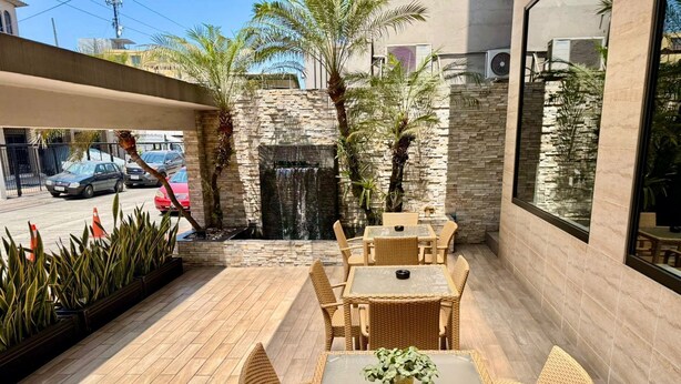 An outdoor patio with wicker furniture, a stone wall, and a water feature. - Hotel Marcelius (Guayaquil)