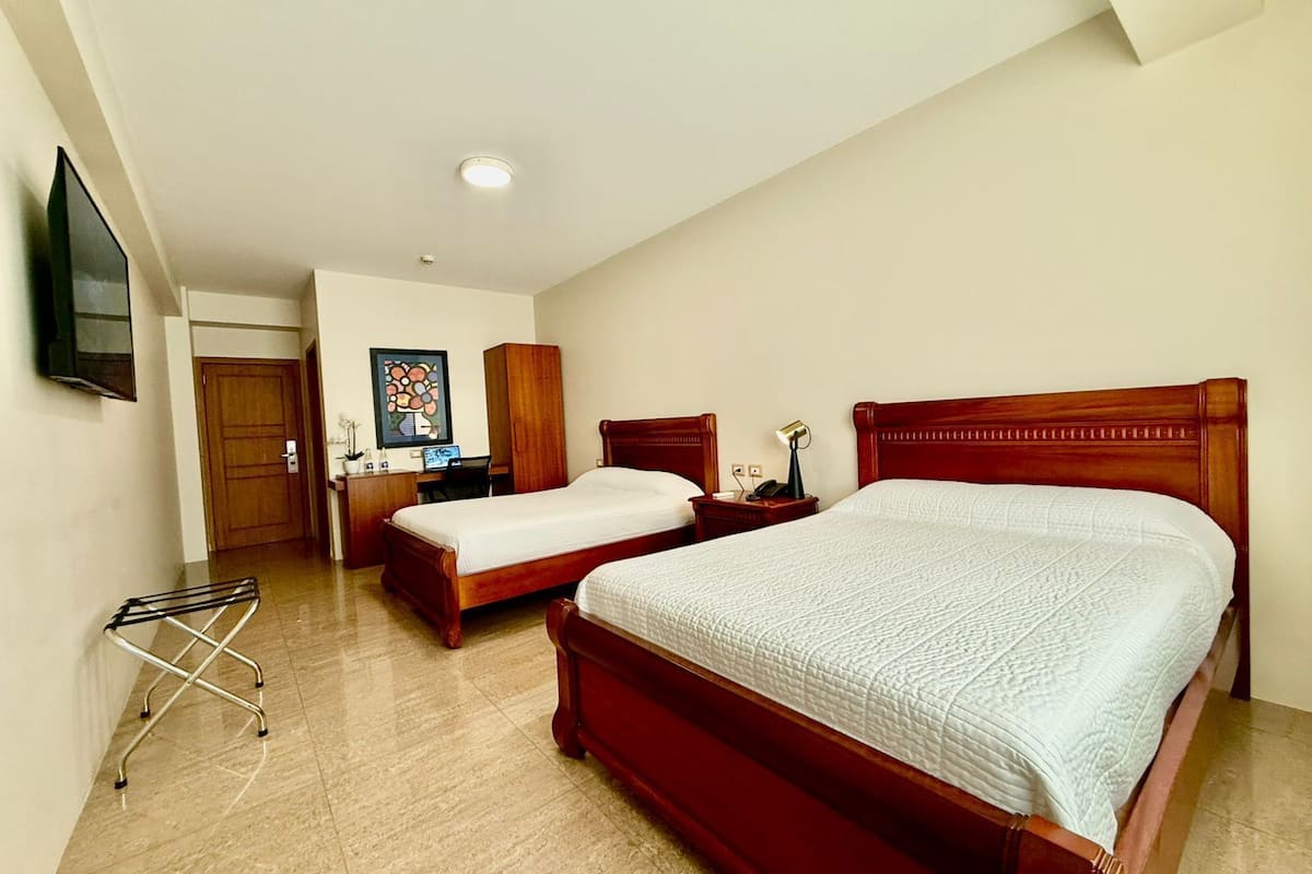 A hotel room with two beds, a desk, a chair, a TV, and a door.