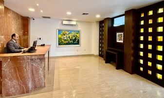 Zona de recepción de un hotel con mostrador de mármol, un cuadro grande y una pared con paneles iluminados.