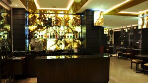 A modern bar area with a marble backlit shelf displaying various bottles, a central bar counter, and seating arrangements. - Hotel Marcelius (Guayaquil)