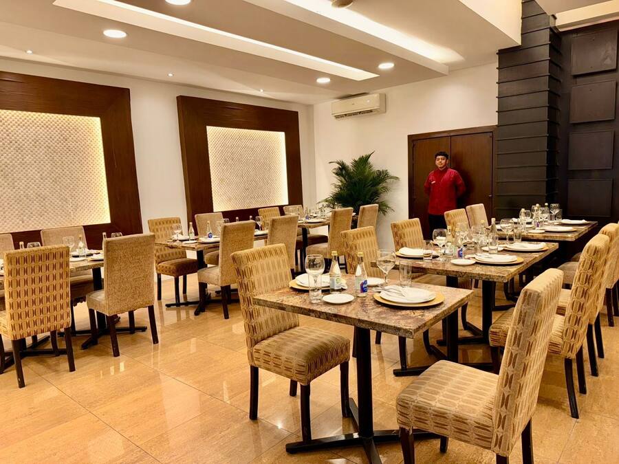 A dining area with multiple tables and chairs, a person standing near the back, and a potted plant.