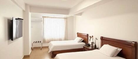 Habitación de hotel con dos camas, un televisor montado en la pared y una ventana con cortinas.