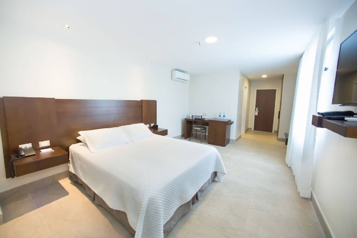 A hotel room with a large bed, a desk, a chair, and a TV.