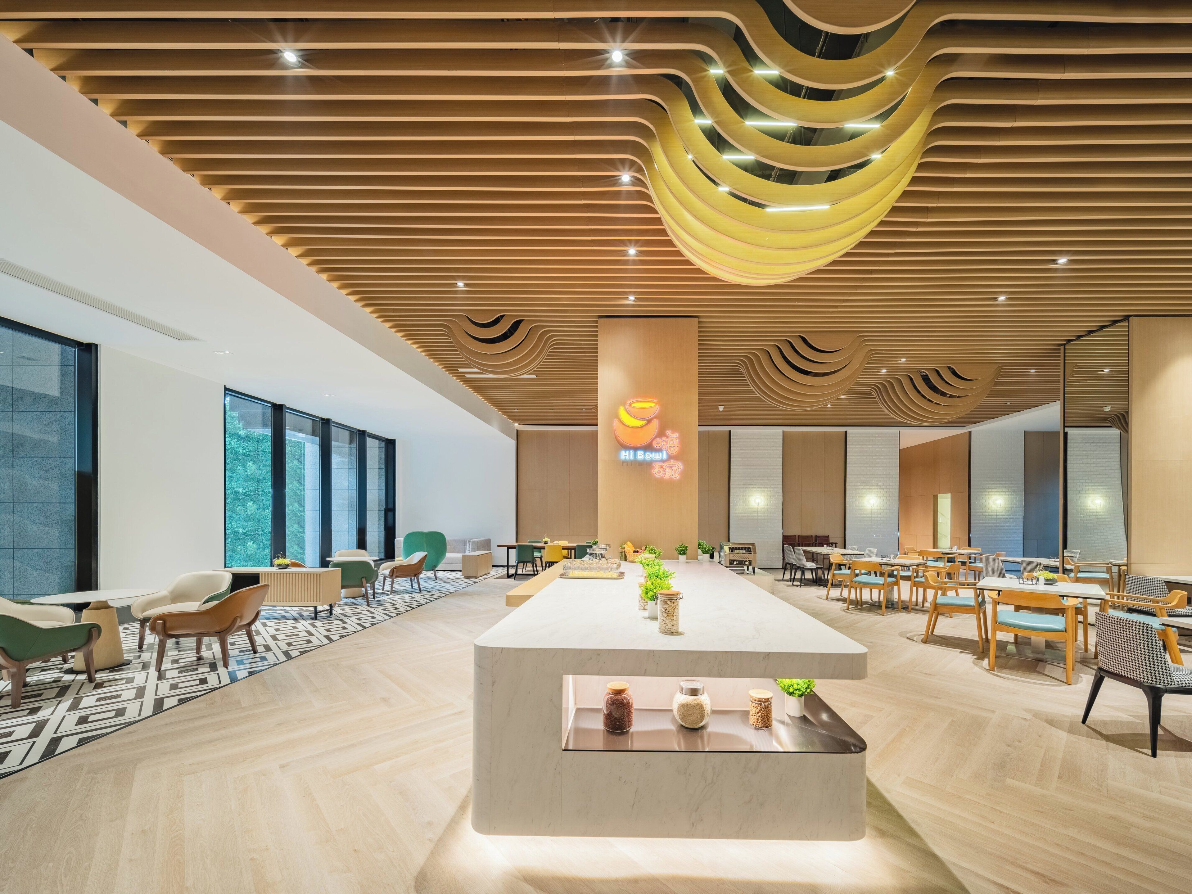 A modern hotel lobby with a central reception desk, seating areas, and large windows offering views.