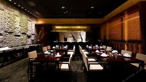 A restaurant with a stone wall, wooden paneling, and a long dining table with chairs.
