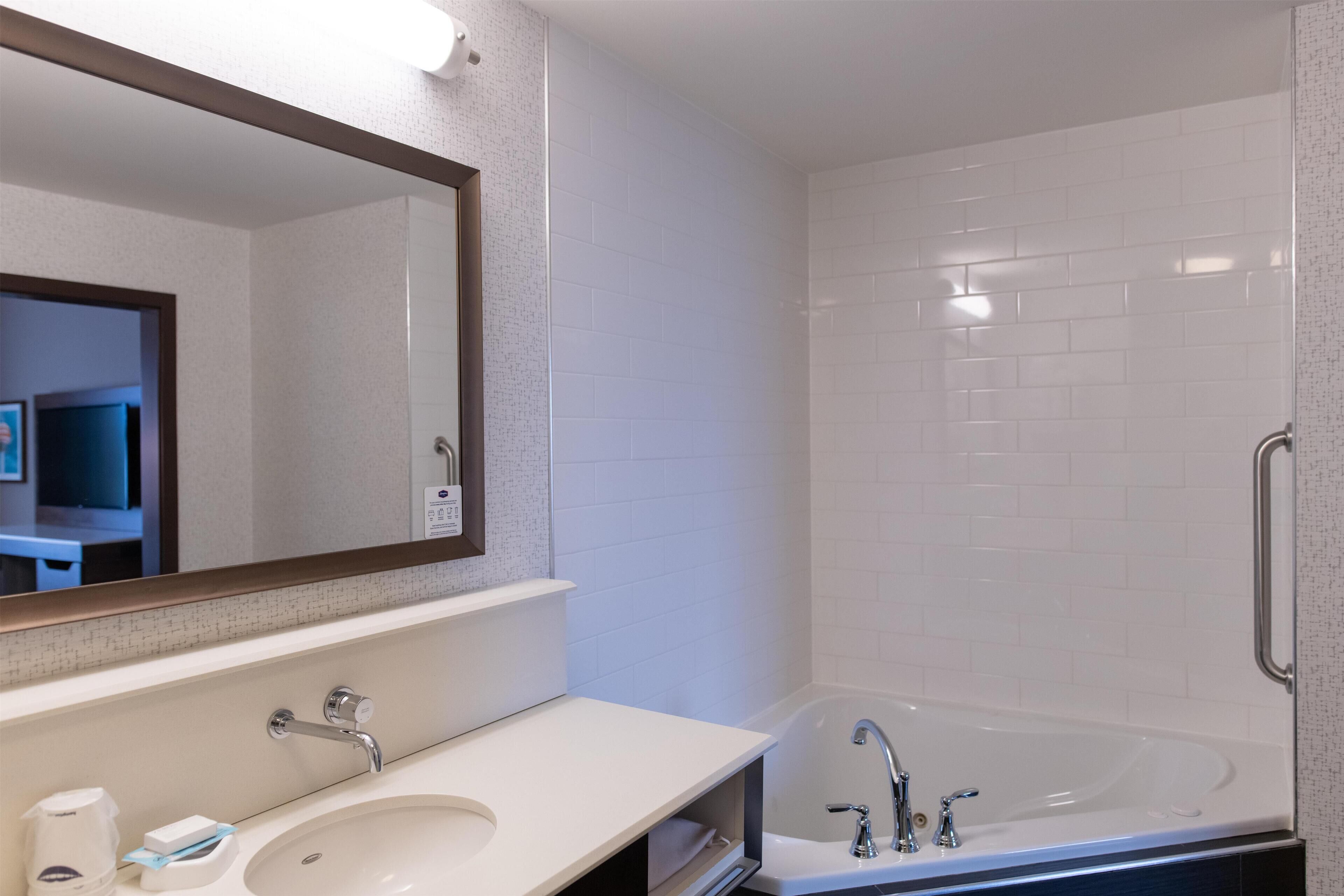 Un baño moderno con un lavamanos, espejo y bañera blancos.