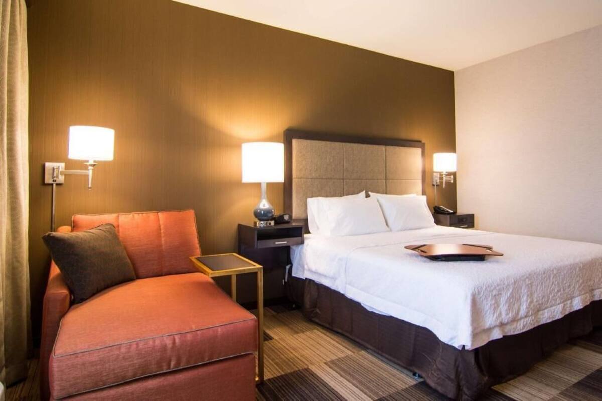 Una habitación de hotel con una cama, una mesita de noche, una lámpara, una silla y una pequeña mesa.