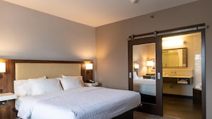 Habitación de hotel con una cama grande, mesitas de noche, un espejo y una puerta corredera hacia el baño.