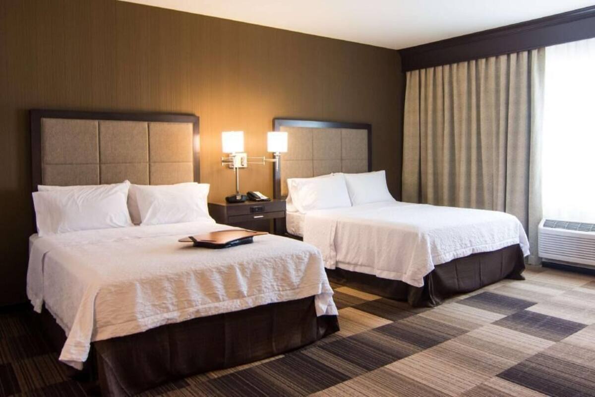 Habitación de hotel con dos camas, una mesita de noche, una lámpara y un equipo de aire acondicionado.