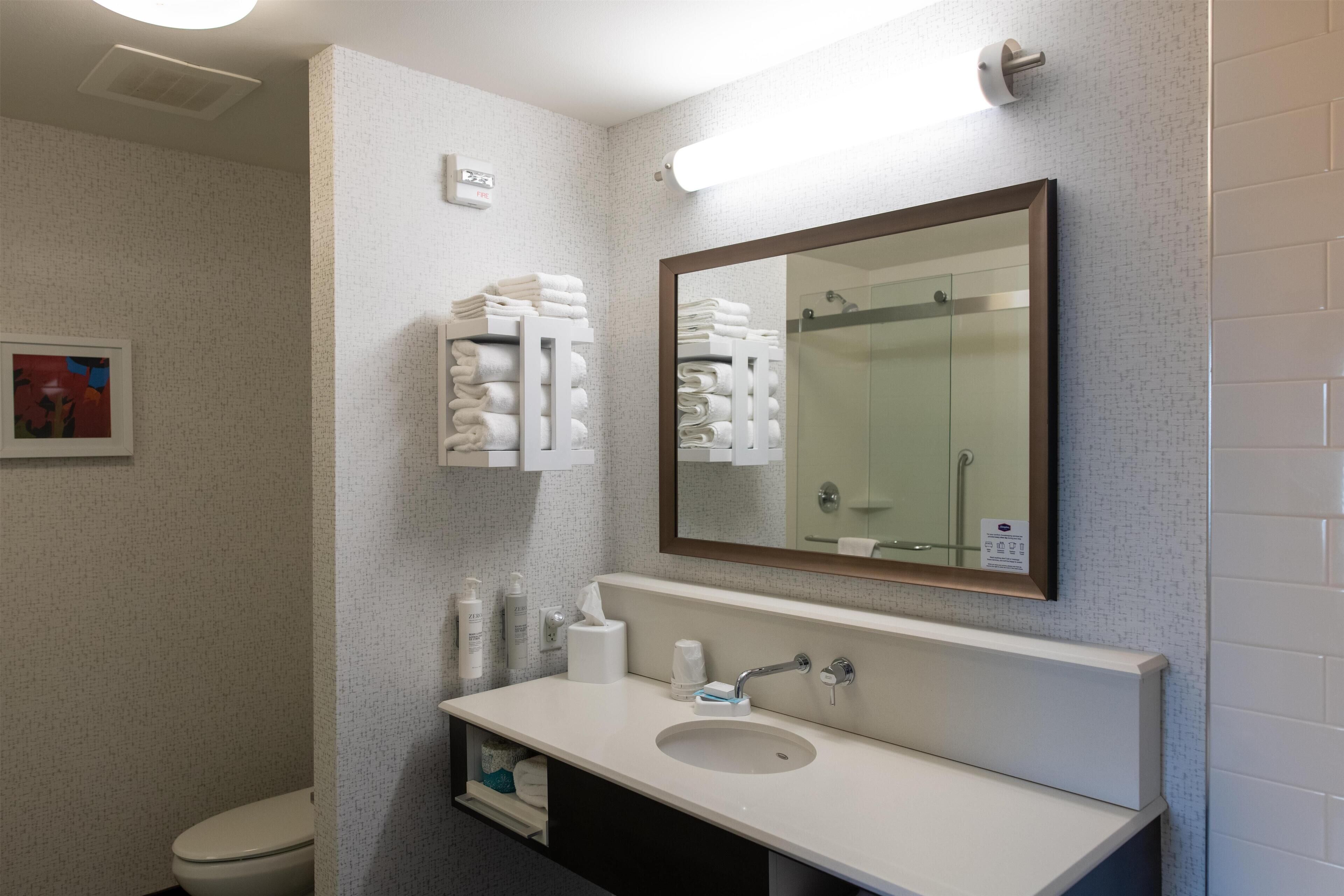 A modern bathroom with a white sink, a large mirror, and neatly stacked towels.