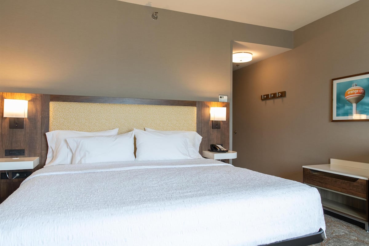 Habitación de hotel con una cama grande, dos mesitas de noche y una lámpara de pared.