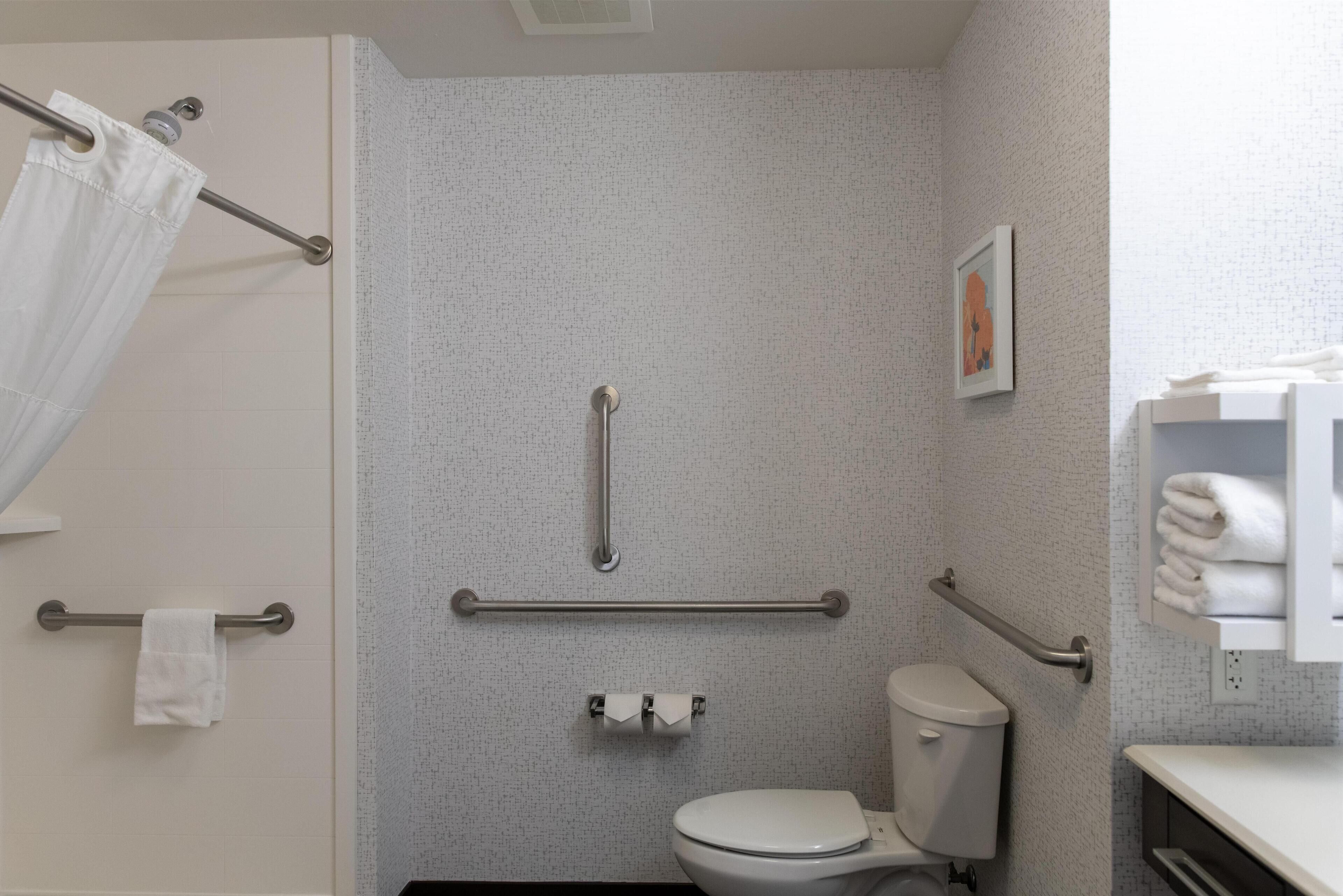 A bathroom with a toilet, grab bars, a towel rack, and a shower curtain.