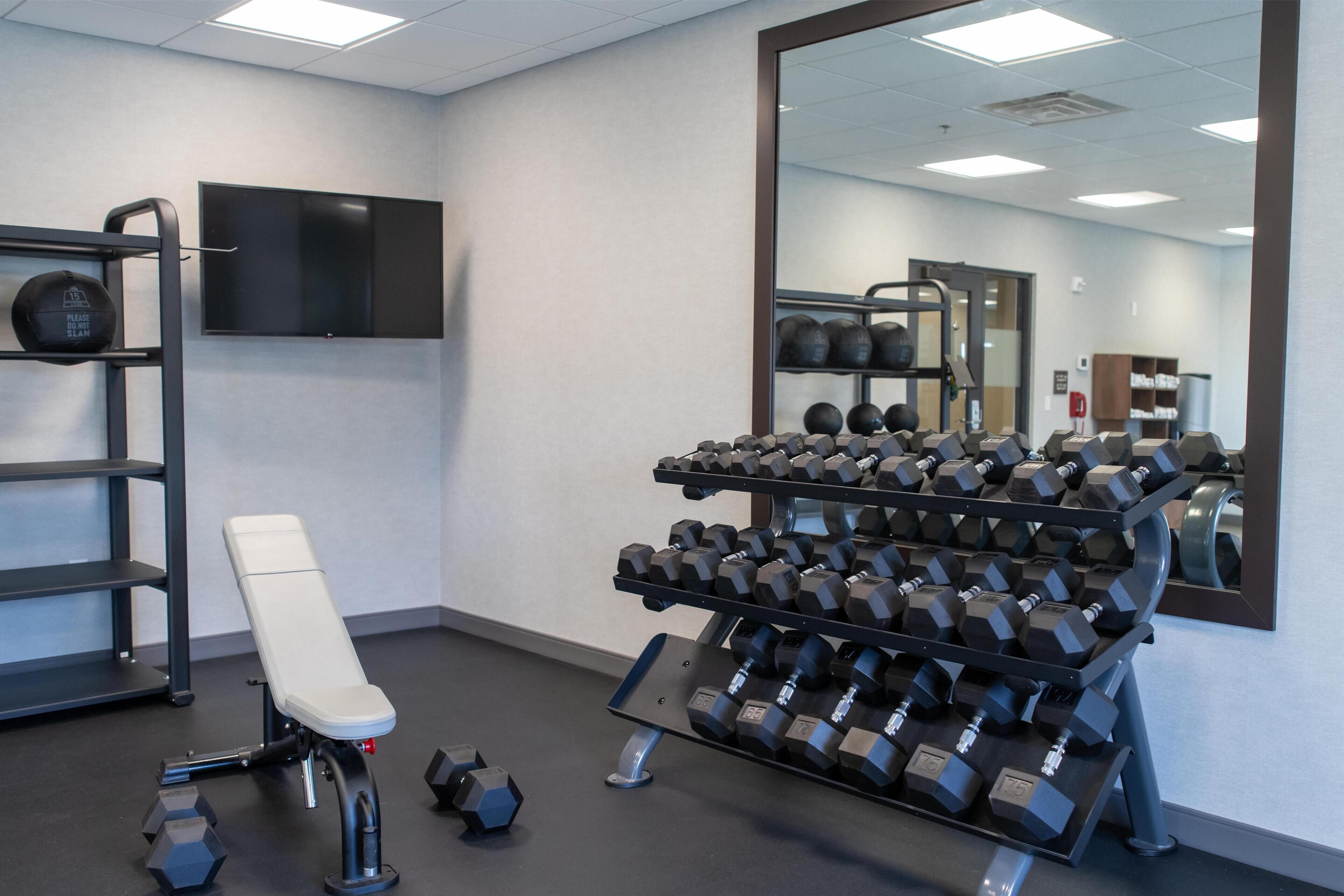 Un gimnasio con una banca, mancuernas y un espejo.