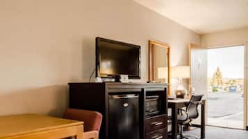A hotel room with a desk, chair, television, refrigerator, and a large window offering a view of the outside.