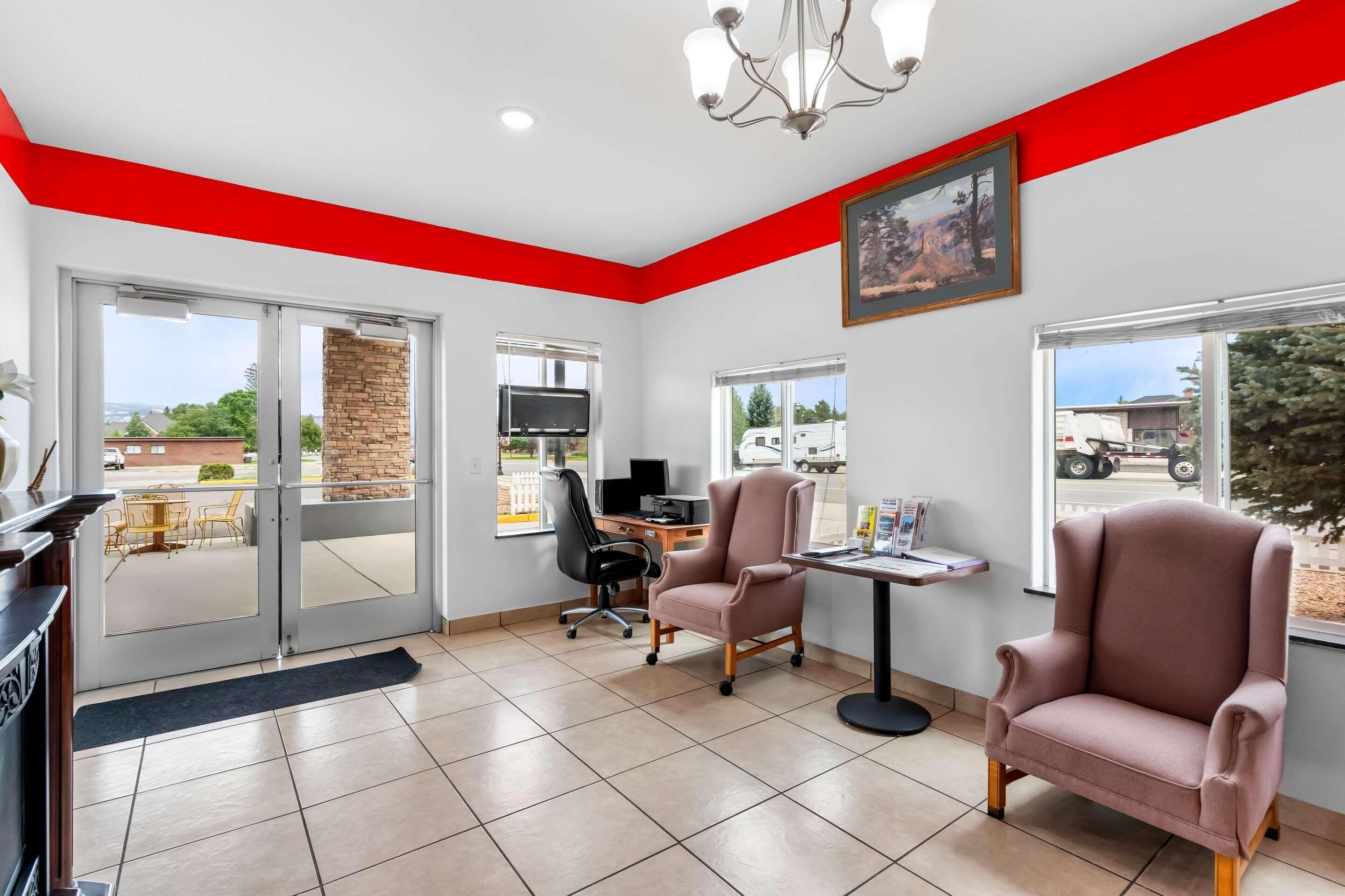 A modern interior with a red accent wall, a fireplace, a desk with a computer, and two armchairs.