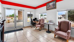 A modern interior with a red accent wall, a fireplace, a desk with a computer, and two armchairs. - Econo Lodge Panguitch Near Bryce Canyon (Panguitch)
