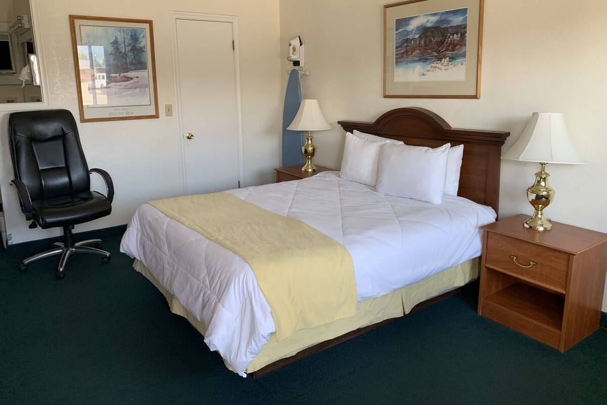 A hotel room with a bed, a chair, a nightstand, and two lamps.