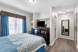 Una habitación de hotel con cama, escritorio con computadora, televisor y espejo.