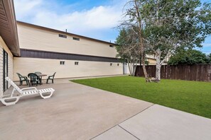 A backyard with a concrete patio, a white lounge chair, and a small table with chairs.