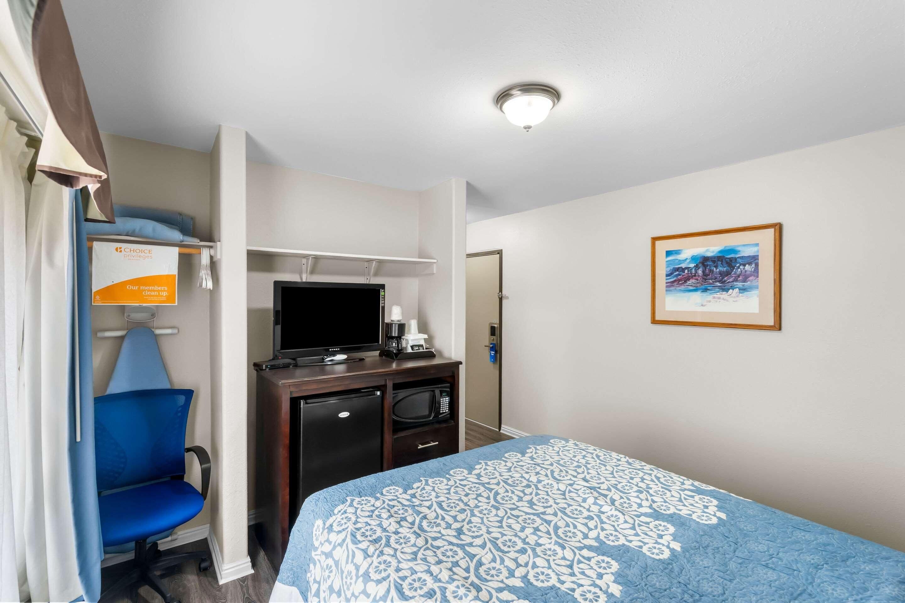 Habitación de hotel con cama, escritorio con computadora, silla, microondas y televisor.