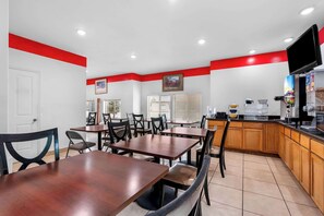 A restaurant with wooden tables and chairs, a kitchen area, and a red accent wall. - Econo Lodge Panguitch Near Bryce Canyon (Panguitch)