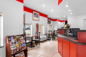 Zona de recepción con mostrador rojo, diversas opciones de asientos y panel informativo turístico.