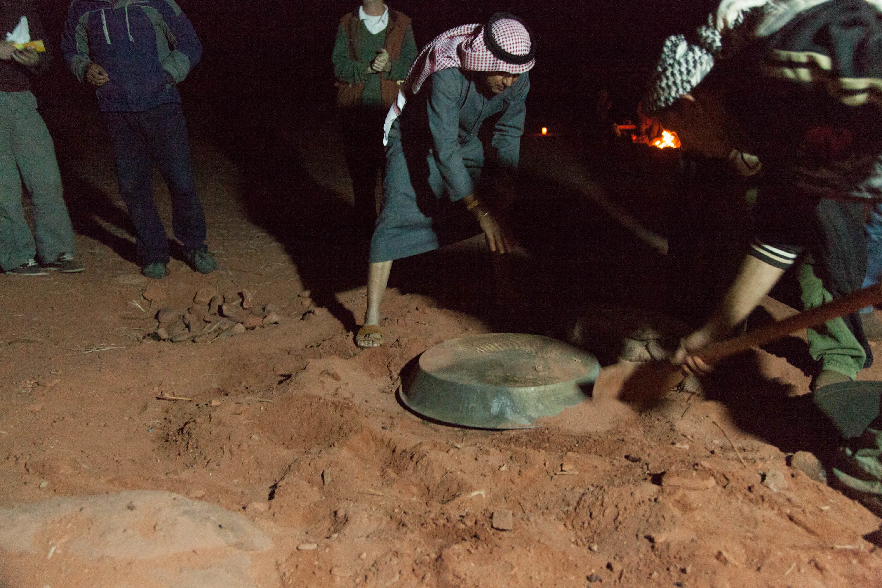 A group of people working with a large metal object on a dirt ground at night.