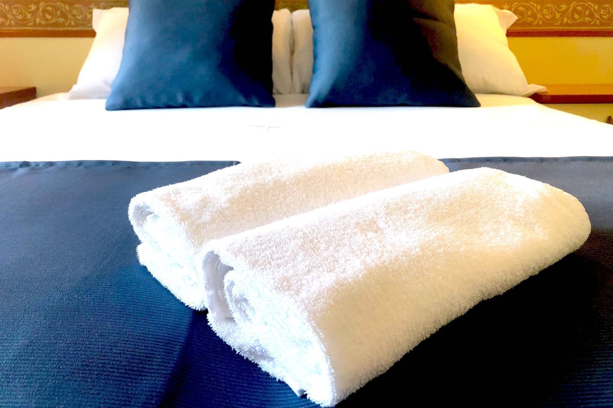 A neatly made bed with a dark blue bedspread and two white towels folded at the foot.