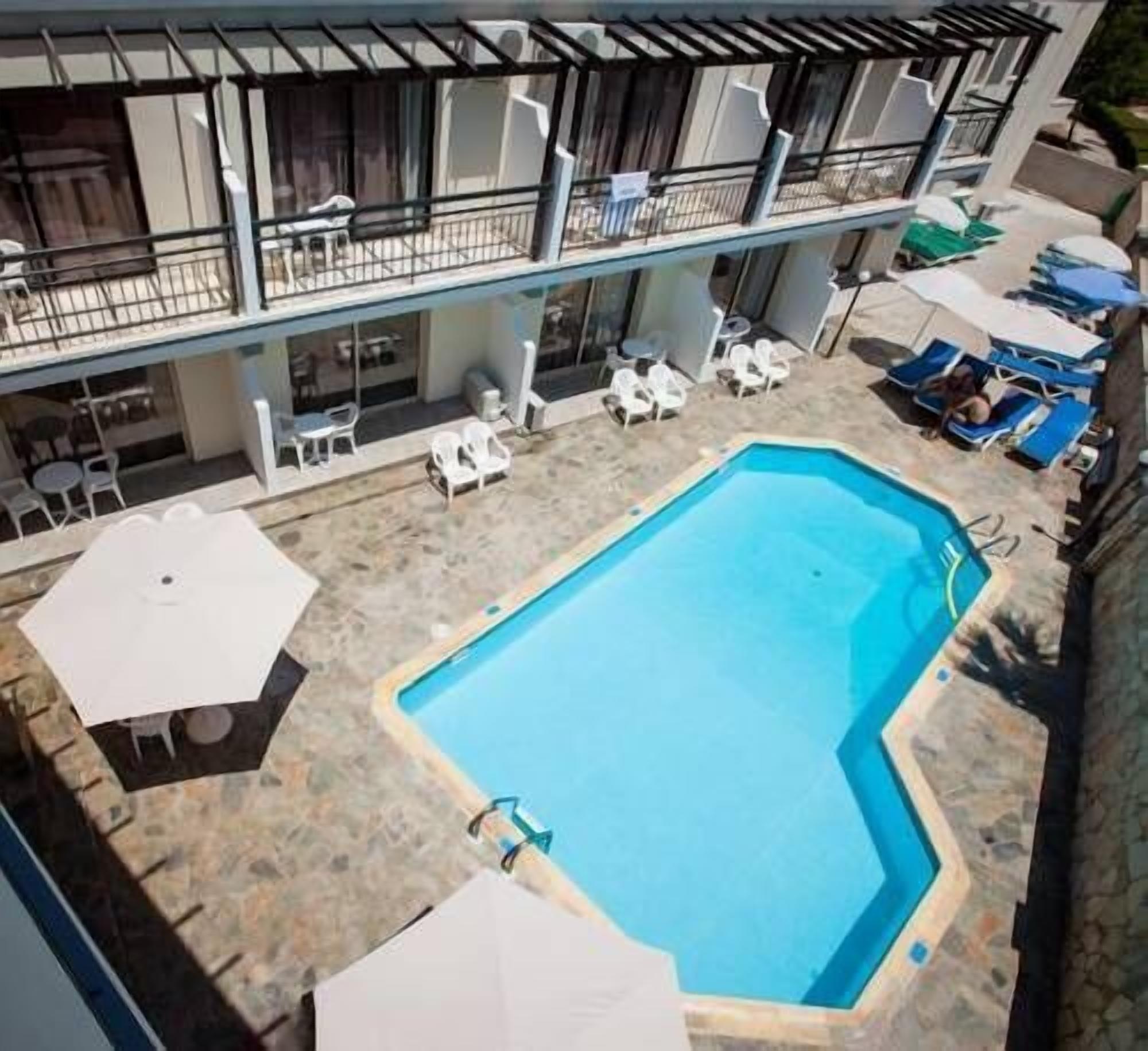 A swimming pool with lounge chairs and umbrellas, surrounded by a building with outdoor seating and a covered area.